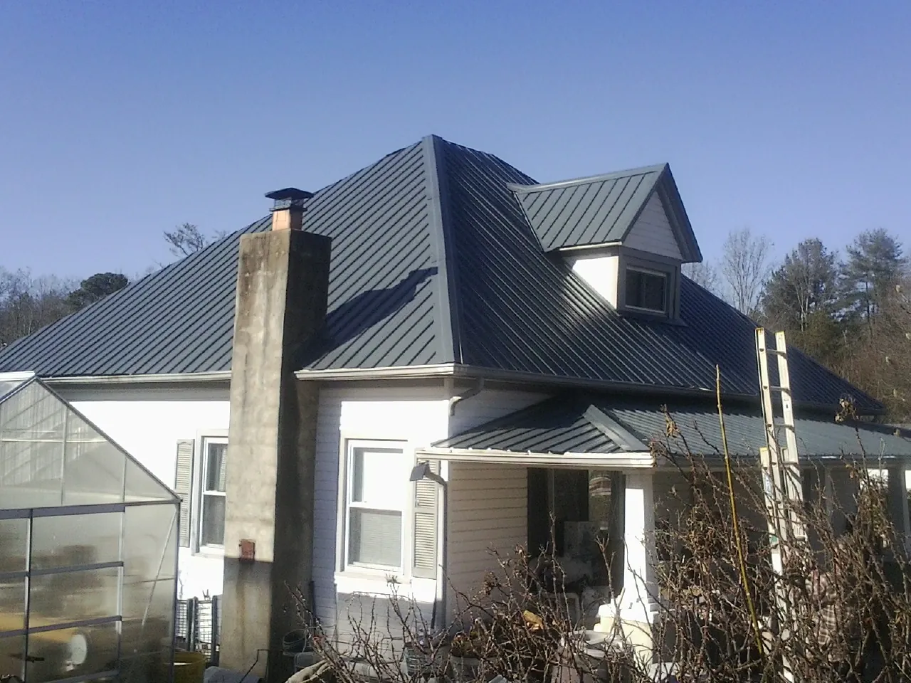 Dark blue standing seam metal roof on a white farmhouse with dormer — Slate & Tile Roof Repair by Roofing Brothers in Travis Afb