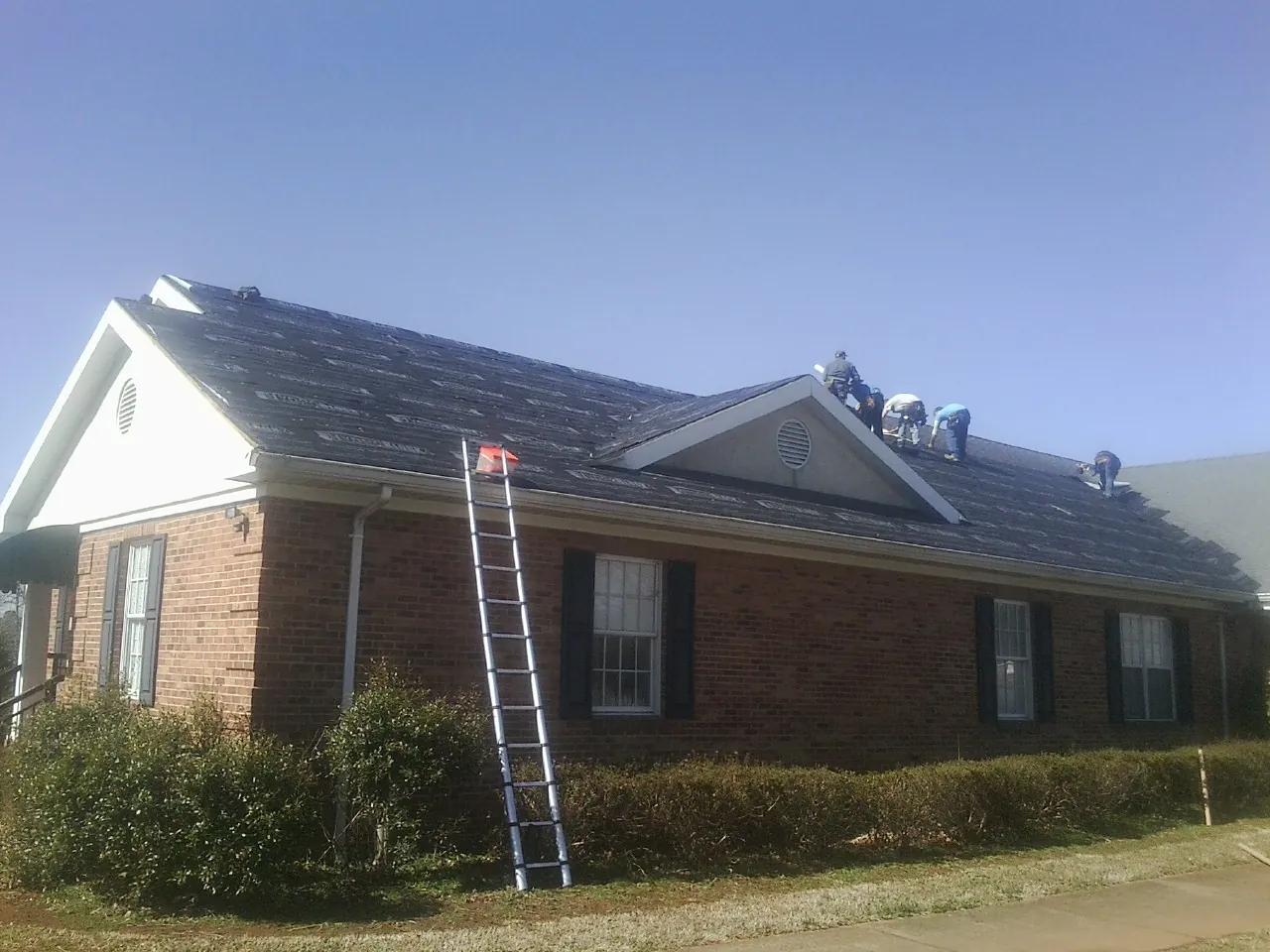 Crew tearing shingles off a brick ranch roof with a ladder set — Emergency Roof Repair work by our crew in Travis Afb