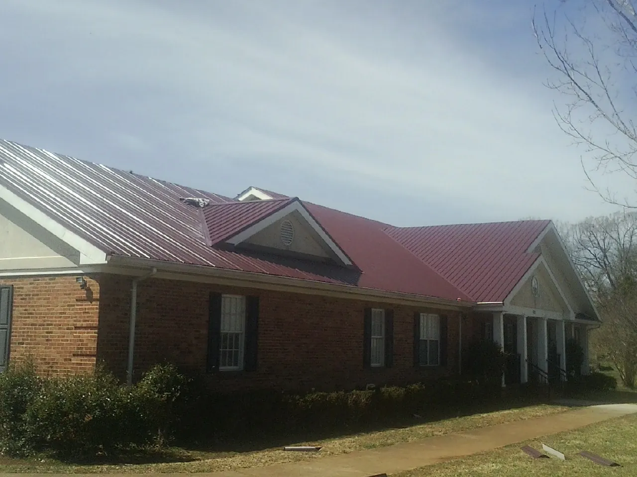 Red metal roof with gabled entries on a long brick building, from a Hail Damage Roof Repair job in Travis Afb
