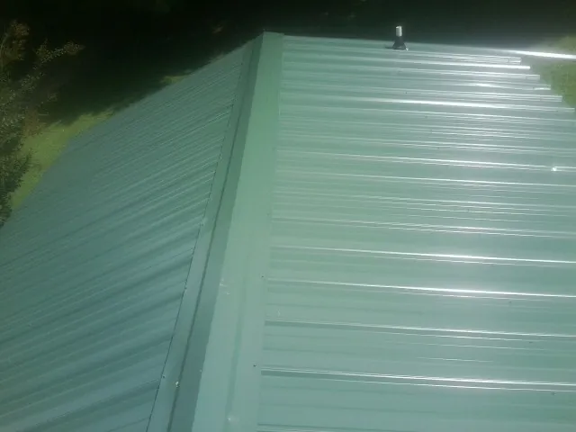New green metal panels meeting at the ridge of a roof — Flat Roof Repair work by our crew in Travis Afb