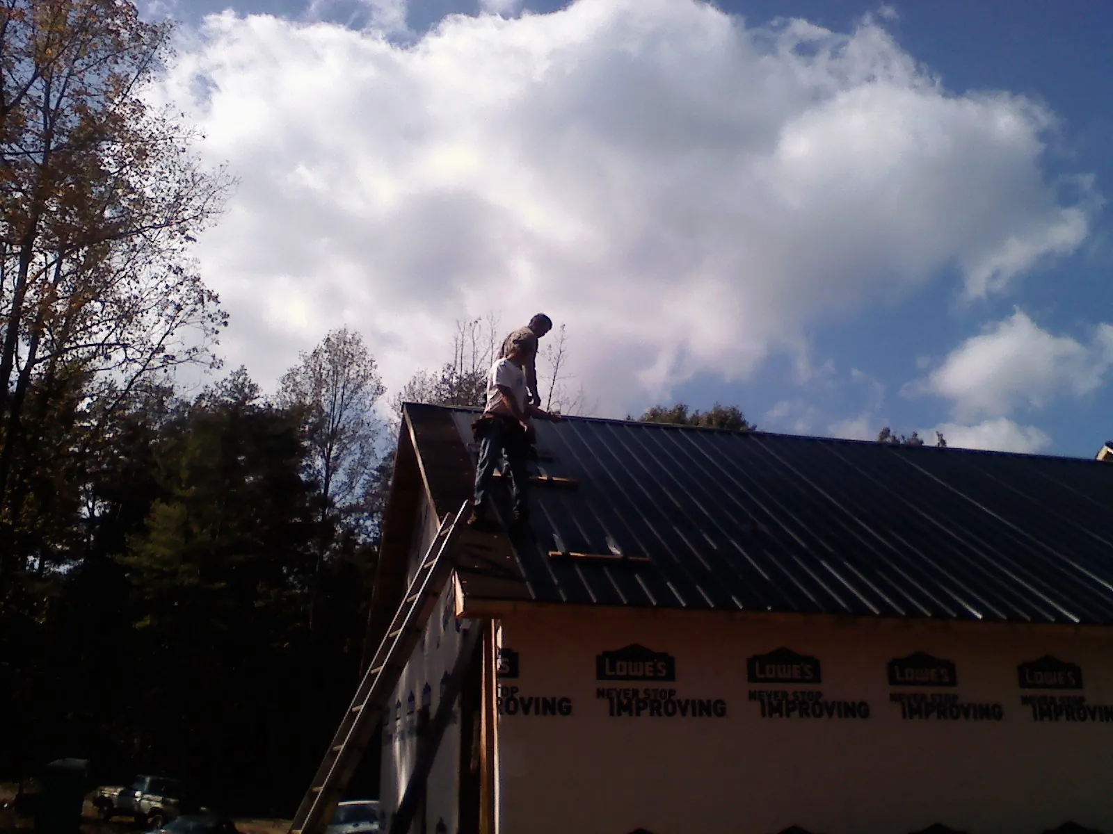 Roofer fastening dark metal panels high against a cloudy sky, from a Roof Inspection job in Travis Afb