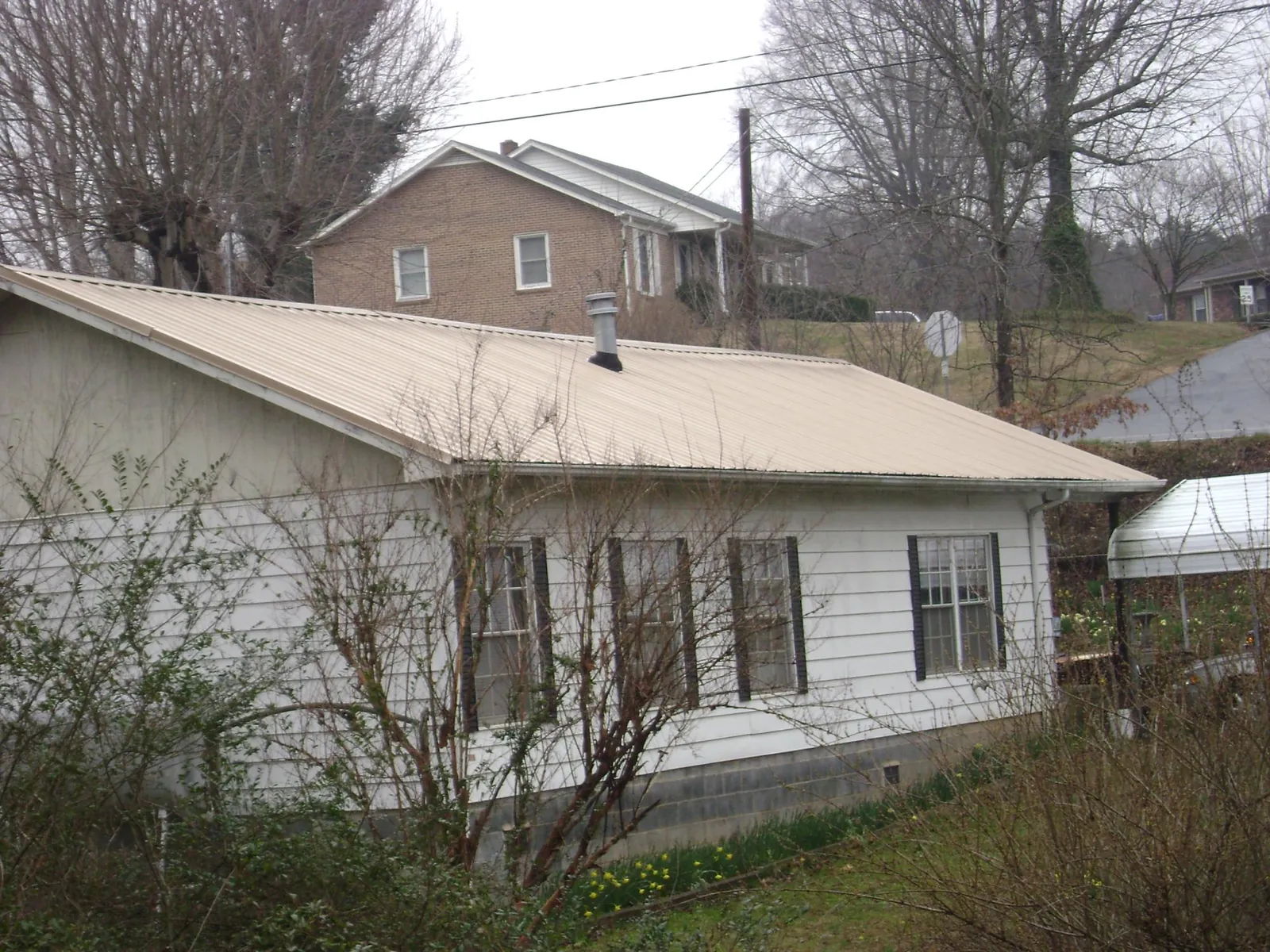 Tan metal roof on a white sided house set into a hillside — Commercial Roofing by Roofing Brothers in Travis Afb